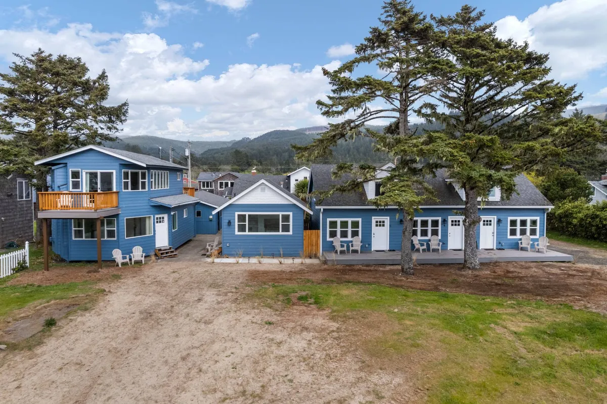 A cheerful outdoor communal area with blue cottages, a spacious seating area, and tall trees with mountains in the background. This lively setting encourages outdoor gatherings and relaxation in nature.