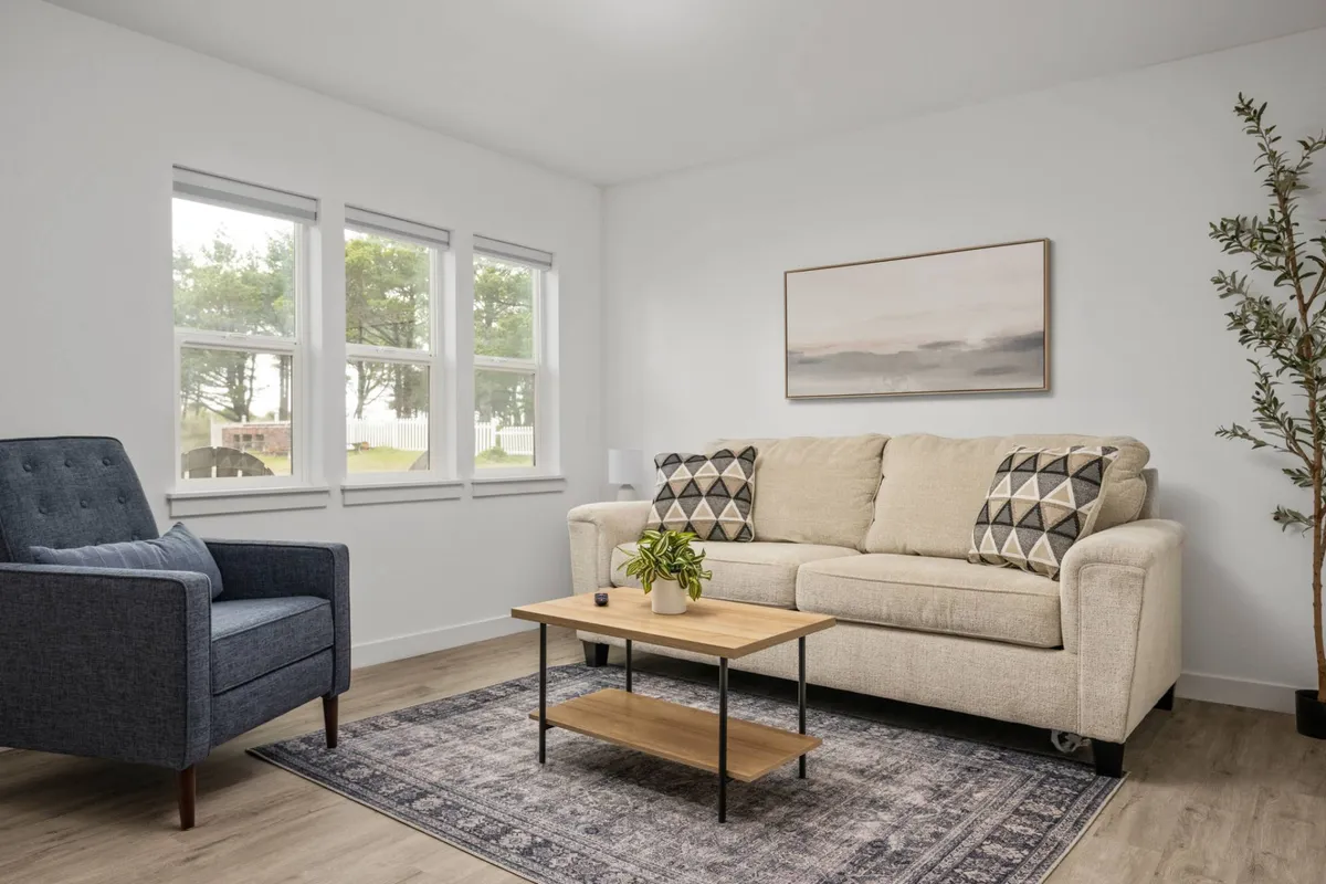 A warm, inviting living area with a comfortable sofa, coffee table, armchair, lush plant, and contemporary artwork. Natural light fills the space, enhancing the cozy atmosphere and highlighting the modern, thoughtful décor.