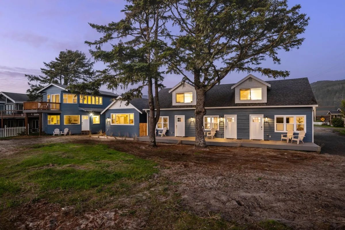An evening exterior image of the main house with glowing windows, a welcoming porch area with seating, and the natural surroundings softly illuminated. The inviting ambiance hints at opportunities for gathering, relaxing, and sharing moments with loved ones after a day of adventure.