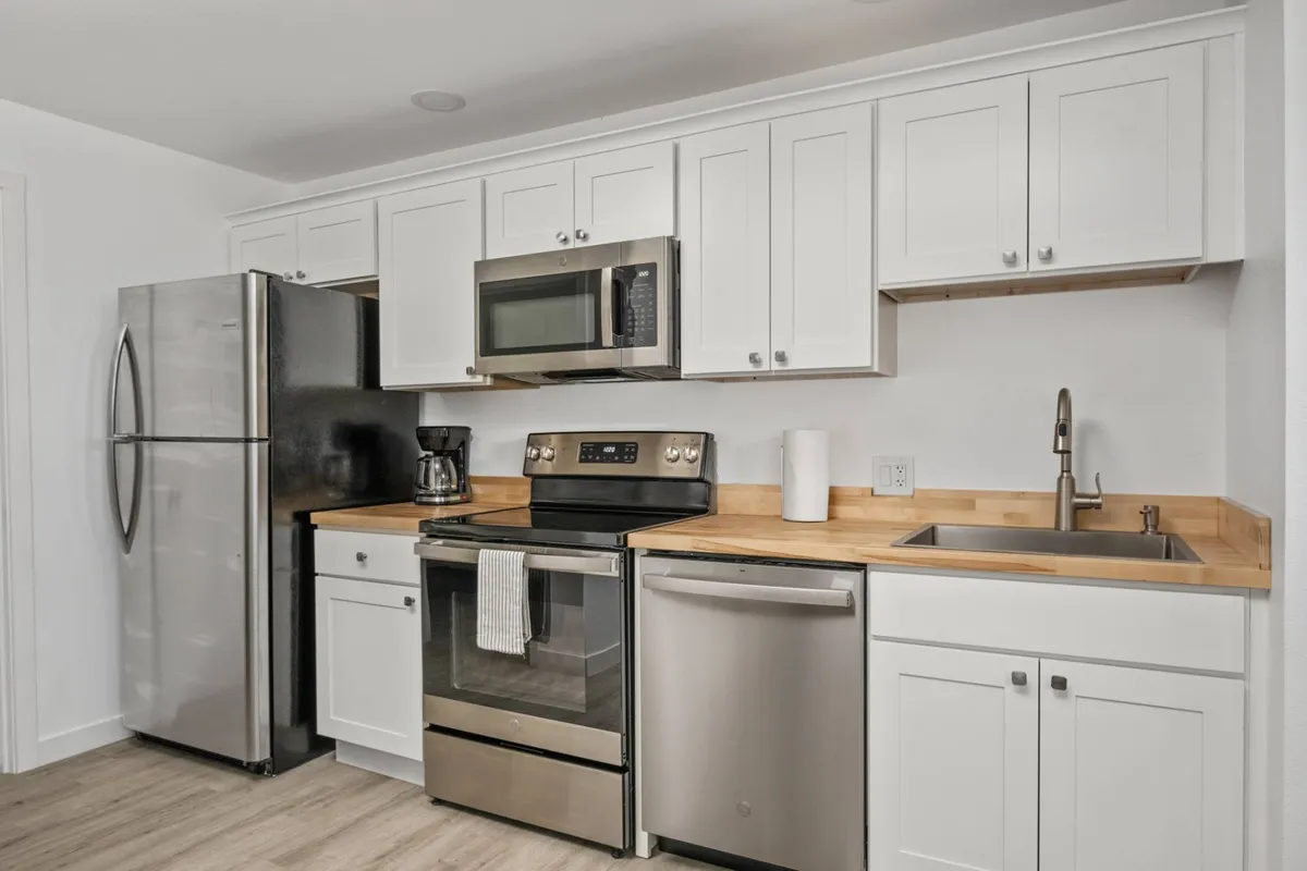 A close-up look at the new, fully equipped kitchen featuring stainless steel appliances, a wooden countertop, and pristine white cabinetry. The scene is inviting for home-cooked meals and social gatherings.