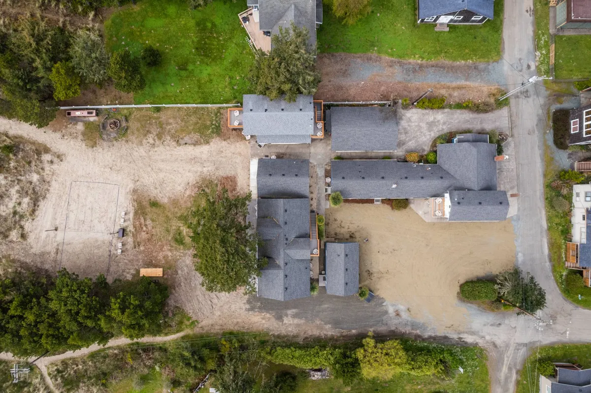 This image captures a wide view of the Ocean Rogue Inn's cluster of buildings nestled among lush greenery, with an open sandy area in the foreground. The relaxed outdoor environment and ample space for activity highlight the property's suitability for community events and gatherings.