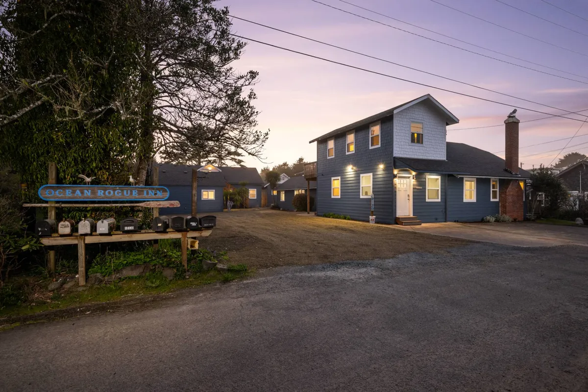 The inviting exterior of the Ocean Rogue Inn, with its charming blue facade, warmly lit windows, and prominent sign. The surrounding area hints at the community atmosphere and proximity to the beach, while the porch offers a welcoming spot for relaxation.
