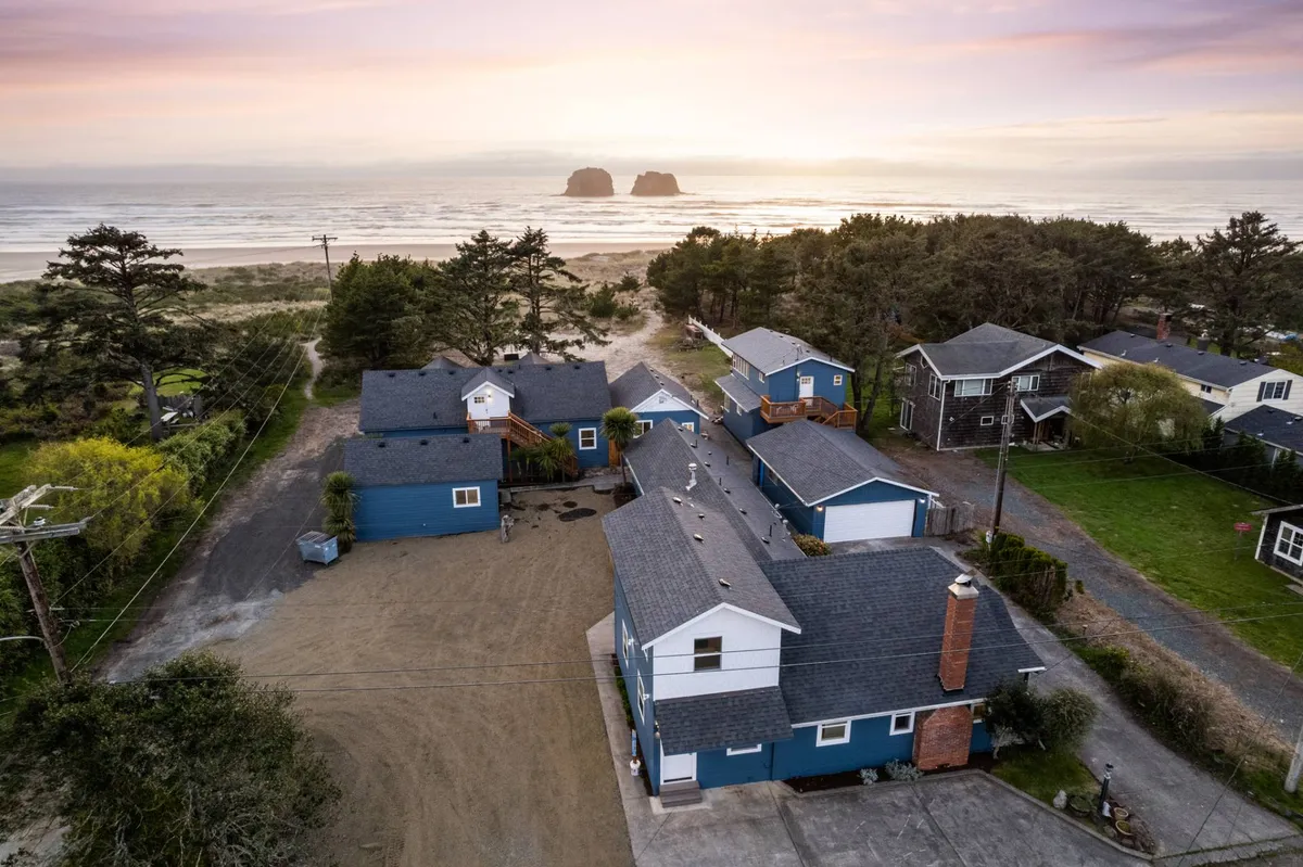 An exterior shot highlighting a sweeping ocean vista, with soft sand, distinctive rock formations, and nearby houses. The scene evokes relaxation, sunset watching, and gatherings along the shoreline, perfect for capturing memories together.