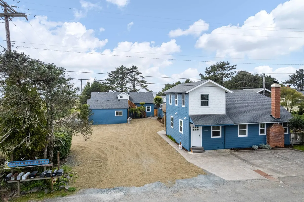 A welcoming view of the blue houses at Ocean Rogue Inn, set against a landscaped yard with a signpost. There's ample outdoor space for family gatherings, outdoor games, and relaxation, echoing the inn's community-centered atmosphere.