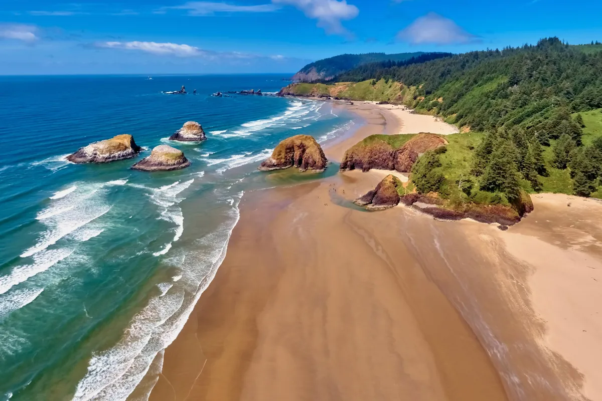 A sweeping beach view with dramatic rock formations, gentle waves, and a sandy shoreline bordered by green hills. The scene is tranquil yet inspiring, ideal for imagining beachcombing, kite flying, and shell hunting adventures.