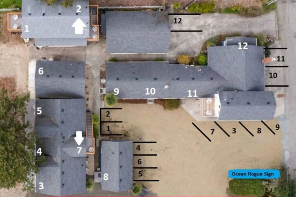 This exterior image shows the Ocean Rogue Inn's multiple buildings arranged around an open communal space, with landscape features, a driveway, and ample room for outdoor activities. The atmosphere is warm and inviting, perfect for gatherings and group events.