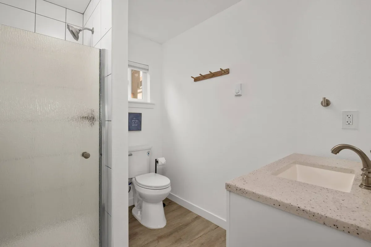 A modern, private full bathroom is depicted with a glass shower, sleek vanity and sink, toilet, and towel rack. The clean, inviting space suggests convenience and comfort after a day at the beach.